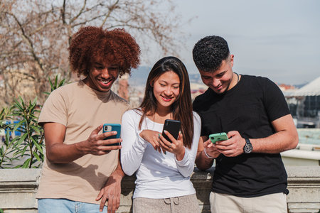 Group of multiracial teenage friends having fun using a cellphone device outdoors. Three multiethinc...