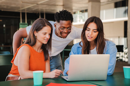 Group of multiracial happy teenage students using laptop, working on university assignment homework project in college library. Meeting of diverse young people looking informationの写真素材