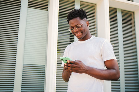 Portrait of smiling young african american man using his smartphone for messaging in social media, watching funny news. Handsome millennial male connecting or browsing on internetの写真素材