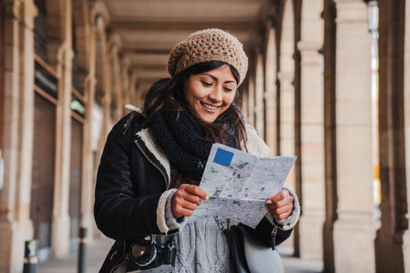 Young tourist woman smiling and reading a map to find the location of the european monument. Lost traveler female walking and watching a trip guide. Lady visiting and sightseeing aの写真素材