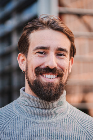Vertical close up portrait of awesome handsome young caucasian male smiling and looking at camera at workplace. Bearded man laughing with friendly expression. Front view of anの写真素材