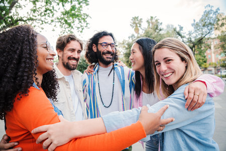 Group of happy people hugging each others on a circle. On foreground one friendly blonde young woman looking at camera and embracing her friends. Cheerful teamwork having fun on aの写真素材