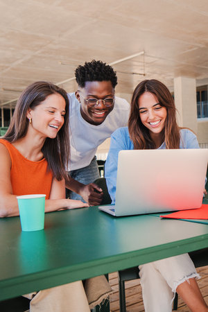 Vertical portrait of a group of multiracial happy teenage students using laptop, working on university homework project in college library. Meeting of young people lookingの写真素材