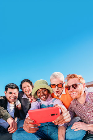 Vertical portrait of group of multiracial happy friends having fun using a cellphone app to browse...