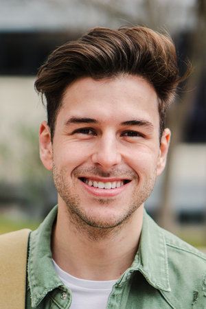 Vertical close up portrait of teenage male student smiling and looking at camera with positive expression standing at college. Handsome caucasian happy male in university campusの写真素材