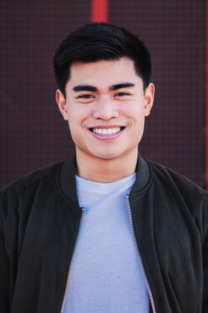 Vertical close up portrait of an asian young guy smiling looking at camera. Isolated teenage male with cheerful expression. Front view of real positive freelance man laughing withの写真素材
