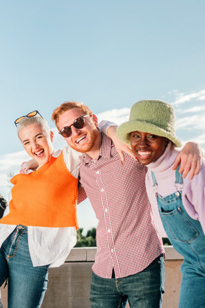 Vertical portrait of a group of young adult people having fun together at summer weekend party. Front view of three multiracial friends smiling and laughing together outsideの写真素材