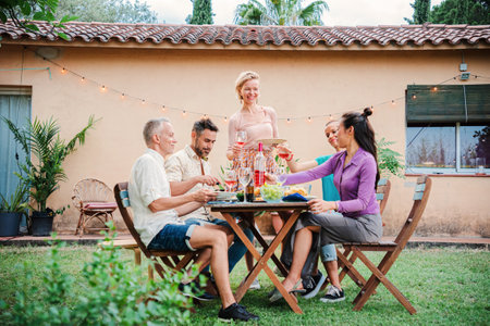 A group of mature adult friends having fun together on a barbeque lunch party at home backyard. Middle aged happy people smiling celebrating a birthday dining reunion with familyの写真素材