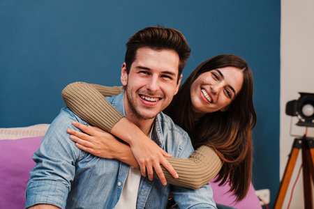 Close up portrait of happy young couple in love, cudding and relaxing in their modern apartment. Smiling wife embracing her husband and looking at camera enjoying their new homeの写真素材