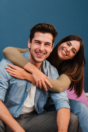 Vertical portrait of happy young couple in love, cudding and relaxing in their modern apartment. Smiling wife embracing her husband and looking at camera enjoying their new homeの写真素材