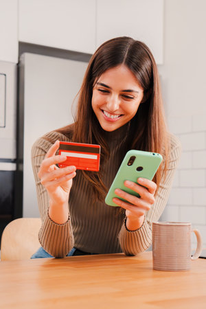 Vertical portrait. Woman using a credit card and a cellphone doing a online shopping transaction,...