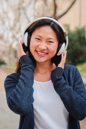 Vertical portrait of one chinese young woman listening music with headphones using wireless...
