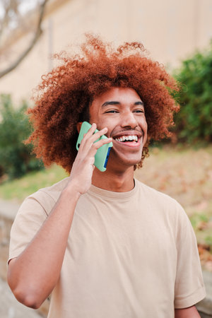 Vertical portrait of young african american guy smiling having a mobile phone call. Happy teenager with toothy smile talking by cellphone. Man laughing on a friendly smartphoneの写真素材