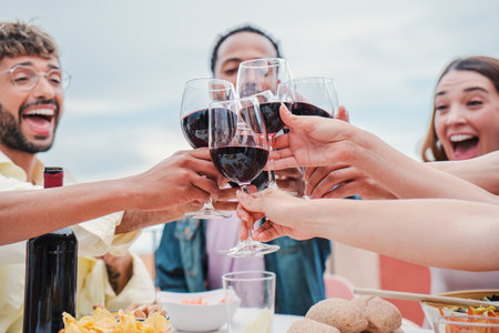 On foreground wineglass. Group of young adult friends toasting or clinking red wine glasses celebrating a birthday party on a winery. Happy people with alcohol and beverage on aの写真素材
