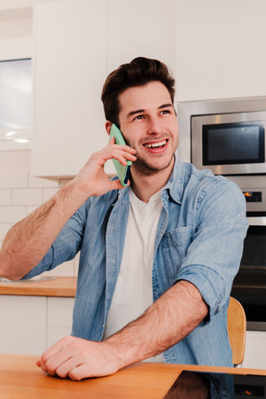 Vertical portrait of young caucasian handsome guy having a friendly telephone call conversation sitting at home with positive expression. One a man smiling, laughing and talking byの写真素材