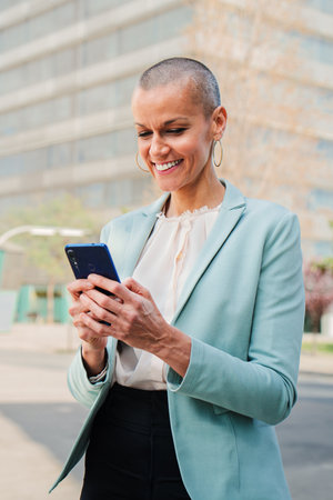 Vertical portrait of a smiling business woman using a mobile phone to browse on internet and share on the social media. Corporate female worker watching successful her stock sharesの写真素材