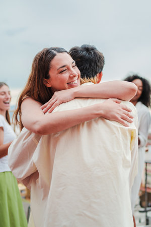 Vertical portrait of a happy young woman giving a hug to her boyfriend on a social festive party with friends. Affectionate couple embracing on a social gathering. Female greetingの写真素材