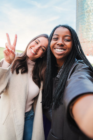 Vertical portrait of a couple of young multiracial women having fun taking a selfie. Front view of...