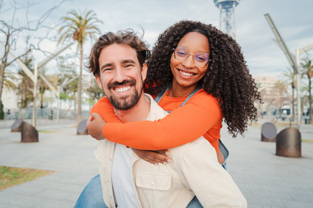 Multiracial real people having fun on a weekend trip. Handsome man giving a piggyback ride to his girlfriend. Married couple embracing together and enjoying together, flirting on aの写真素材