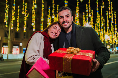 Young caucasian couple smiling and holding a christmas present with a ribbon. Two happy friends giving a surprise bithday gift. Boyfriend and girlfriend showing a traditionalの写真素材