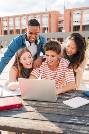 Vertical. Group of young classmates studying together and preparing a exam using a laptop, browsing on internet at university campus. Teenage students smiling and doing theの写真素材
