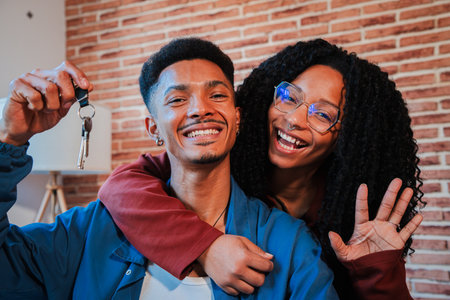 Young african american couple showing keys of their first house after purchase and moving to new home together. happy husband and wife hugging in their apartment excited to beの写真素材