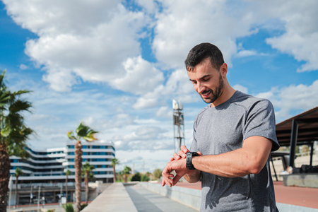 Active Young Energetic Sports Man Checking His Progress on Smart Watch Gear During Outdoor Running...
