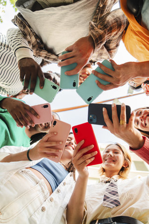 Vertical low angle view of a big group of smiling multiracial teenagers addicted to smart phones, watching funny videos, shopping online, enjoyingの写真素材