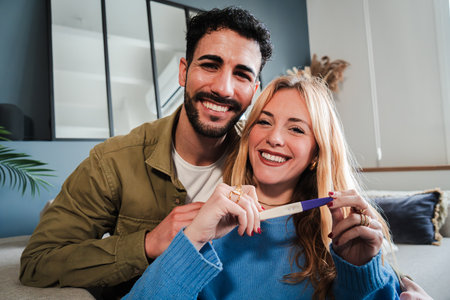 Caucasian couple holding a pregnancy test and looking at camera with a happiness expresion. Husband...