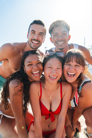 Vertical group of multiracial young friends taking a selfie portrait on the beach wearing swimsuit on their summer vacation. Friendly people shootingの写真素材