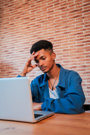 Vertical. Exhausted and stressed African American man working on a laptop at home, suffering from a...