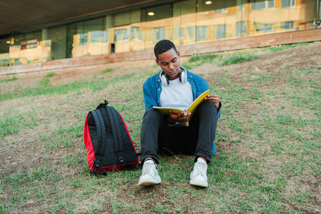 African american handsome guy reading a note book to prepare a exam. Teenage student sitting on the...