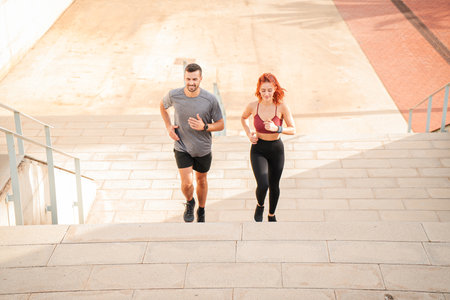 A sporty couple running up stairs to improve their leg muscles. Two athletic young friends doing...