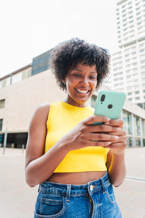 Vertical. African american girl smiling using a cellphone to browse on internet with an app. Teenage...