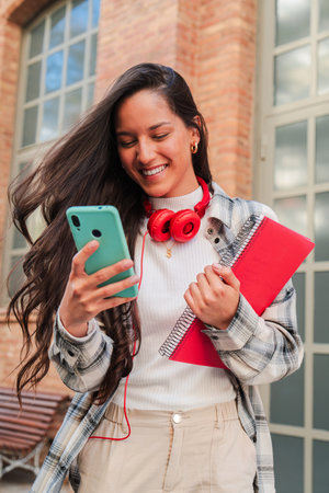 Vertical. One latina student using her smartphone to share on the social media app. Hispanic teenager having fun with a cellphone, Latin femaleの写真素材
