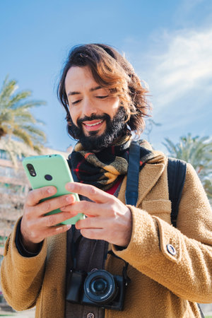 Vertical Happy bearded man using a cellphone app for browsing on internet. Tourist guy smiling and looking for location using a smart phone mapの写真素材