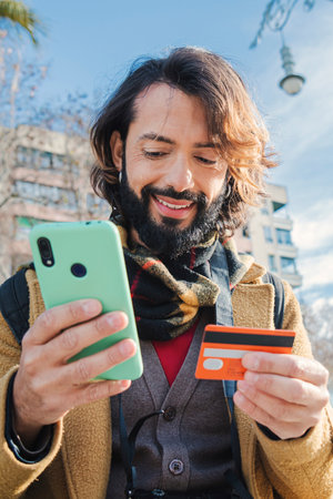 Vertical young man paying a purchase with a credit card and holding a smart phone device standing...