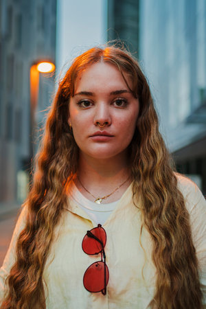Vertical. Close up portrait of a young woman looking at camera. One serious female staring front at night. Unhappy teenage girl with pensiveの写真素材