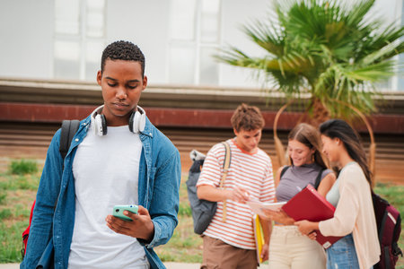 Serious african american teenage student using a cellphone at university campus. Isolated guy watching bad news on his smartphone on the high schoolの写真素材