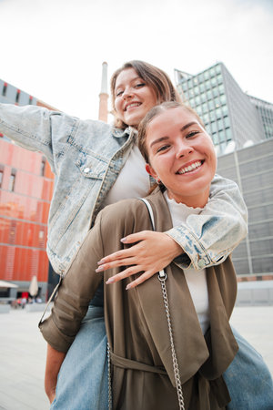 Vertical. Cheerful young woman giving her friend a piggyback ride while laughing and having fun together outdoors, showing happiness, friendship, andの写真素材