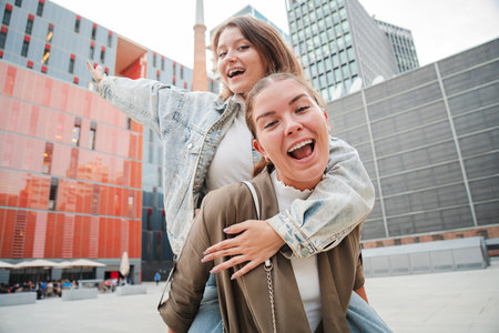 Cheerful young woman giving her friend a piggyback ride while laughing and having fun together outdoors, showing happiness, friendship, and playfulの写真素材