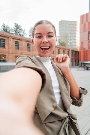 Vertical. Young adult woman smiling while taking a selfie with a cellphone, showcasing her joyful personality. Close up portrait of a teenage girlの写真素材