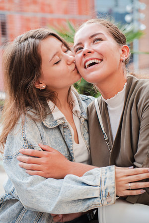 Vertical. Joyful moment of affection between two female friends as one gives a sweet kiss on the cheek, sharing happiness, closeness, and friendshipの写真素材
