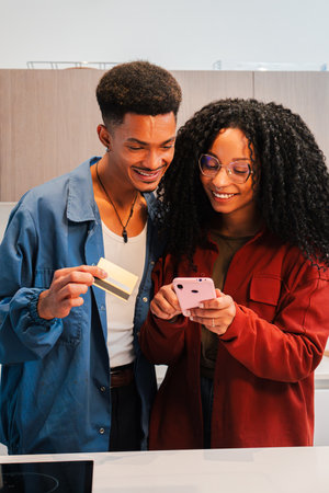 Vertical. Happy couple using a credit card and smartphone to shop online in a bright kitchen, enjoying a moment of togetherness while managing theirの写真素材