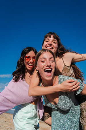 Three Joyful Female Friends Enjoying a Fun Day at the Beach with Laughter and Smiles While Embracing the Spirit of Freedom Under a Bright Blue andの写真素材