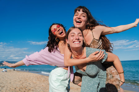 Three Joyful Female Friends Enjoying a Fun Day at the Beach with Laughter and Smiles While Embracing the Spirit of Freedom Under a Bright Blue andの写真素材