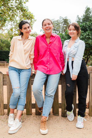 Three Beautiful Young Women Are Laughing Joyfully in a Scenic Outdoor Park. They Are Dressed in Casual Attire Smiling Brightly and Posing Togetherの写真素材