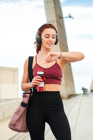 Active and enthusiastic girl checking the time on her smart watch while holding a water bottle,...