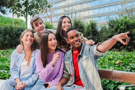 A lively group of cheerful friends joyfully sharing laughter and pointing at something interesting while enjoying a delightful day together in anの写真素材