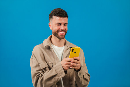 Young man joyfully interacting with a yellow smartphone while enjoying his leisure time and smilingの写真素材